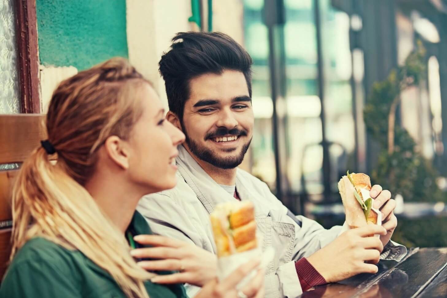 A man and woman sitting at a table with sandwiches.